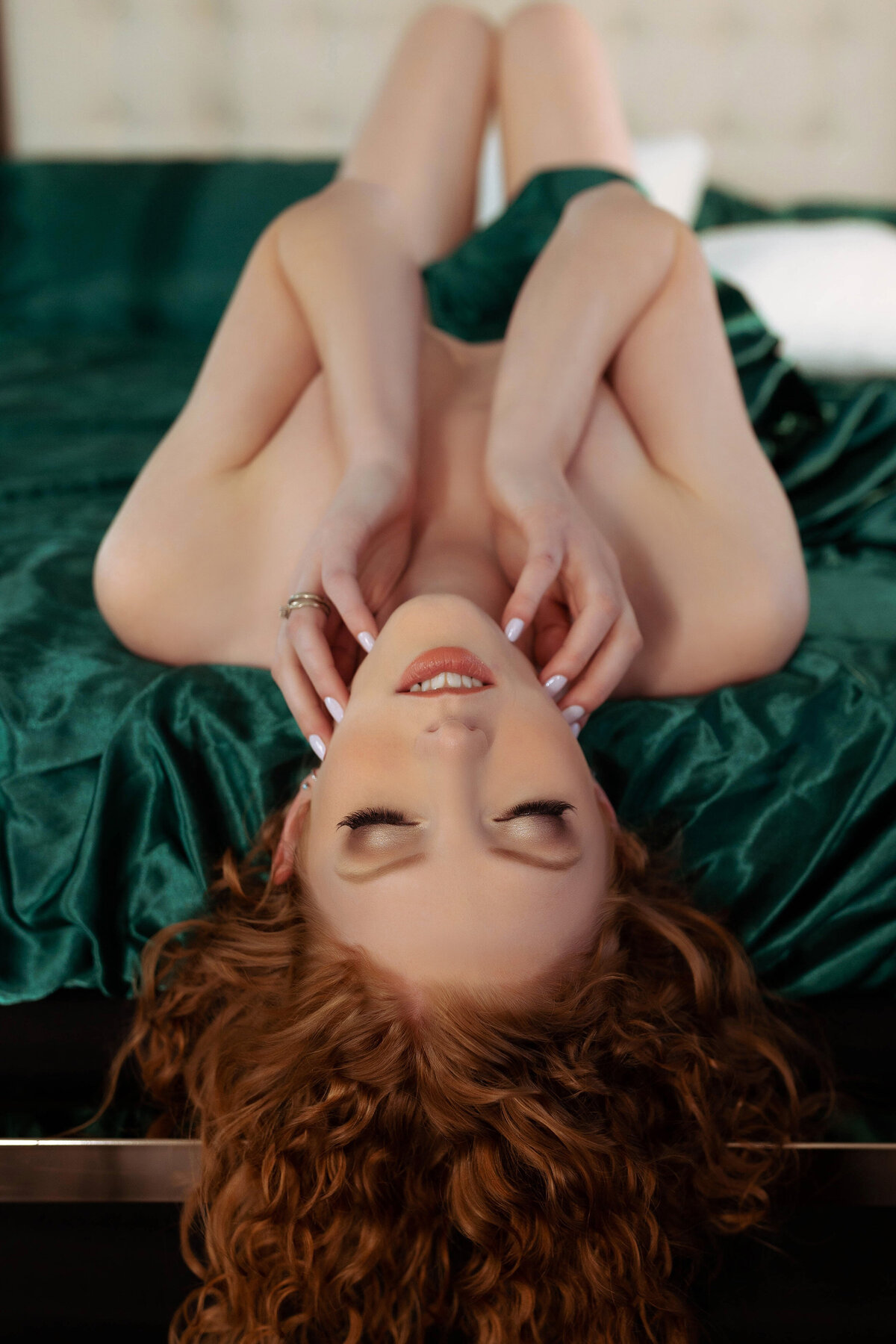 redhead woman wearing green sheets laying on bed with hands on face