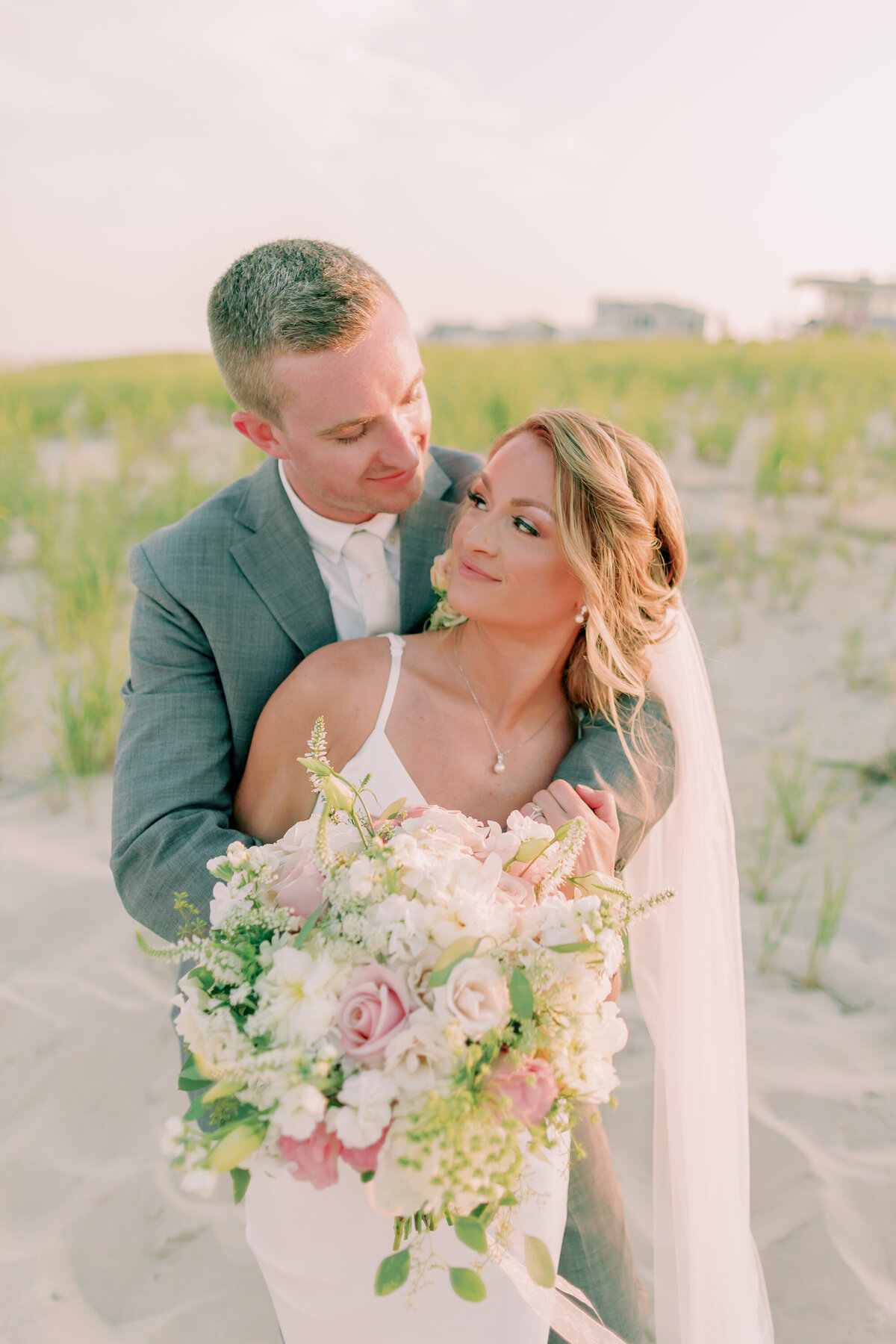 A newlywed standing behind their partner with their arms wrapped around them as they look at each other 