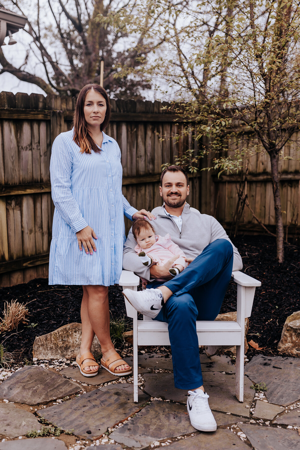 Nashville family photographers captures father holding baby while sitting down while wife stands next to chair