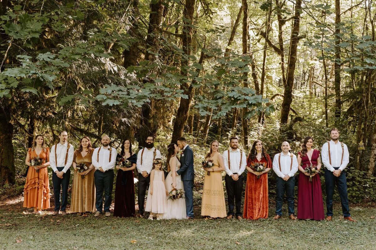 Large wedding party with fall colored dresses and all holding bouquets or wearing a boutonniere by Eugene florist Flowers and Thyme.