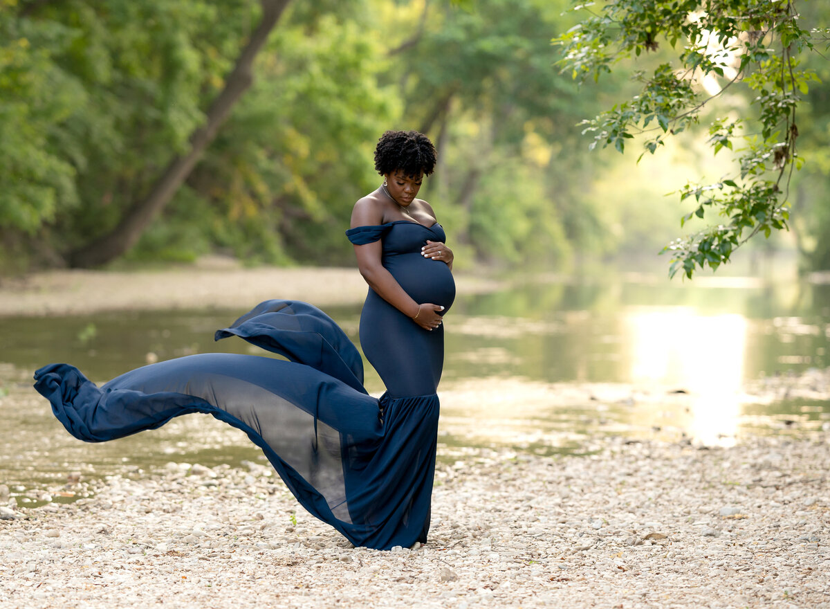 pregnant woman wearing blue mermaid gown by a creek