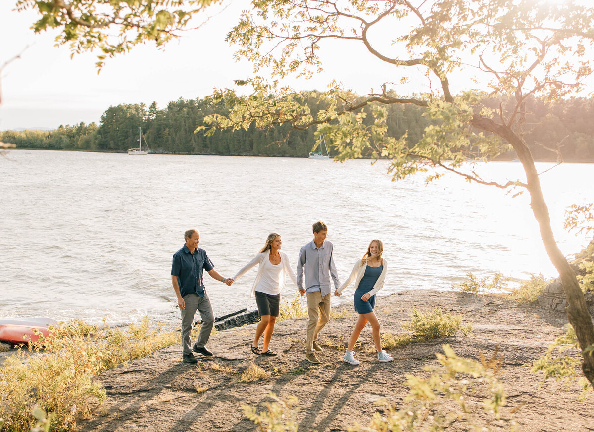 A Family holding hands and walking along the rocky water line of lake champlain 