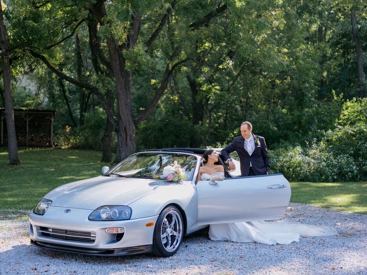 Bride and groom beside their favorite sports car on their wedding day.