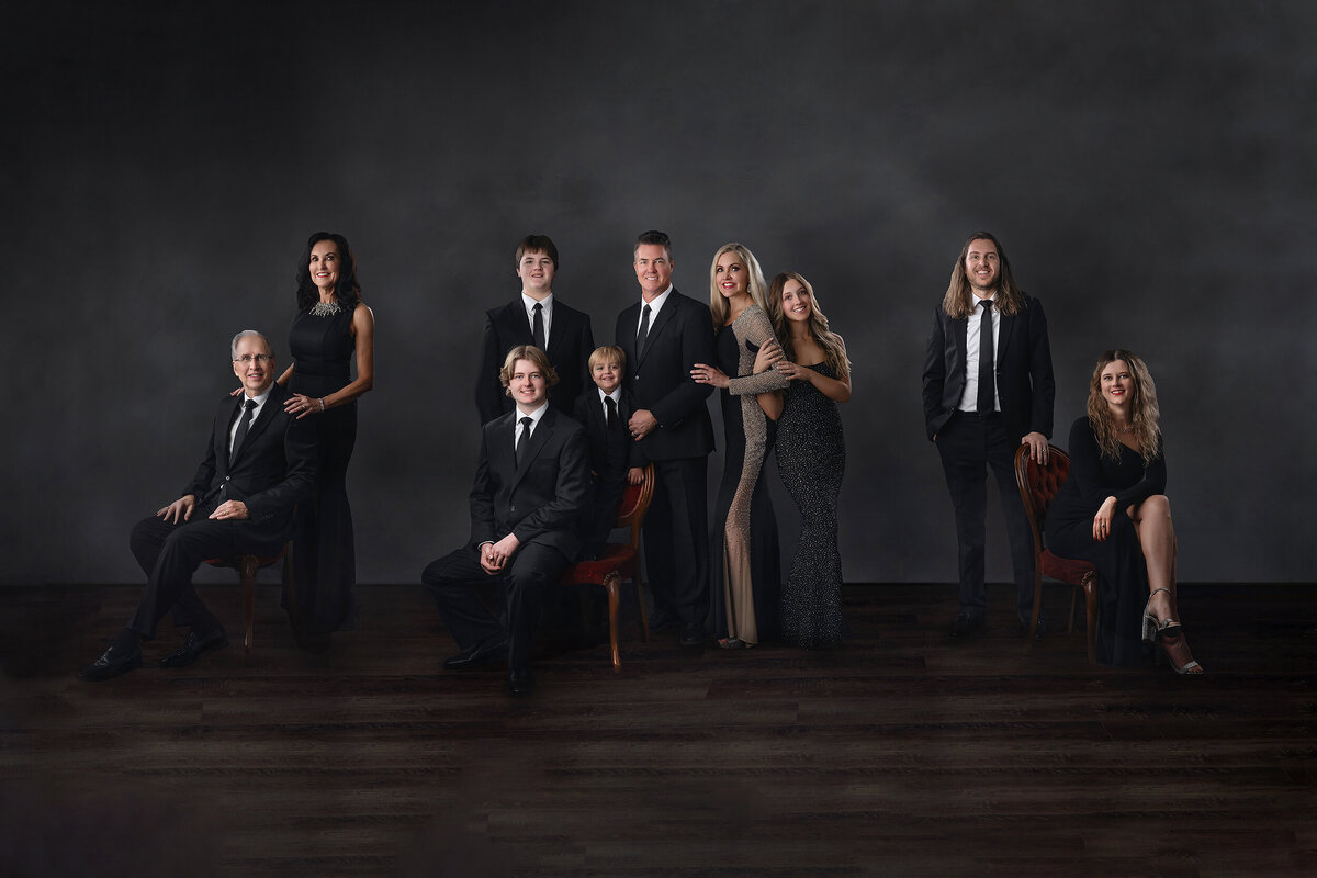 A formal family portrait features an elegantly dressed group in black-tie attire against a classic dark studio backdrop.