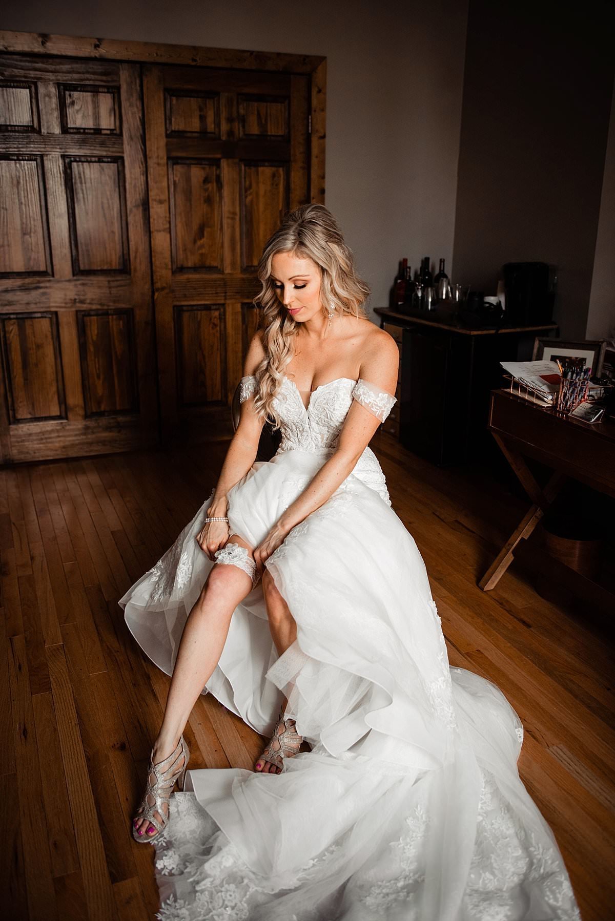 Bride sitting in bridal room pulling her garter up her leg