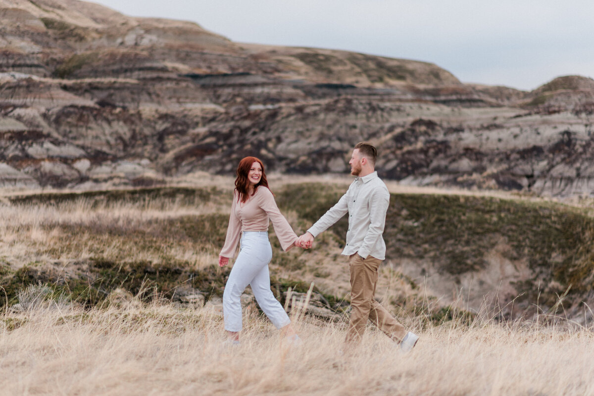 Couple holds hands, walking through grass in the Badlands of Alberta.