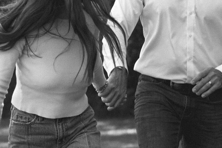 black and white closeup of a man and woman holding hands while running.