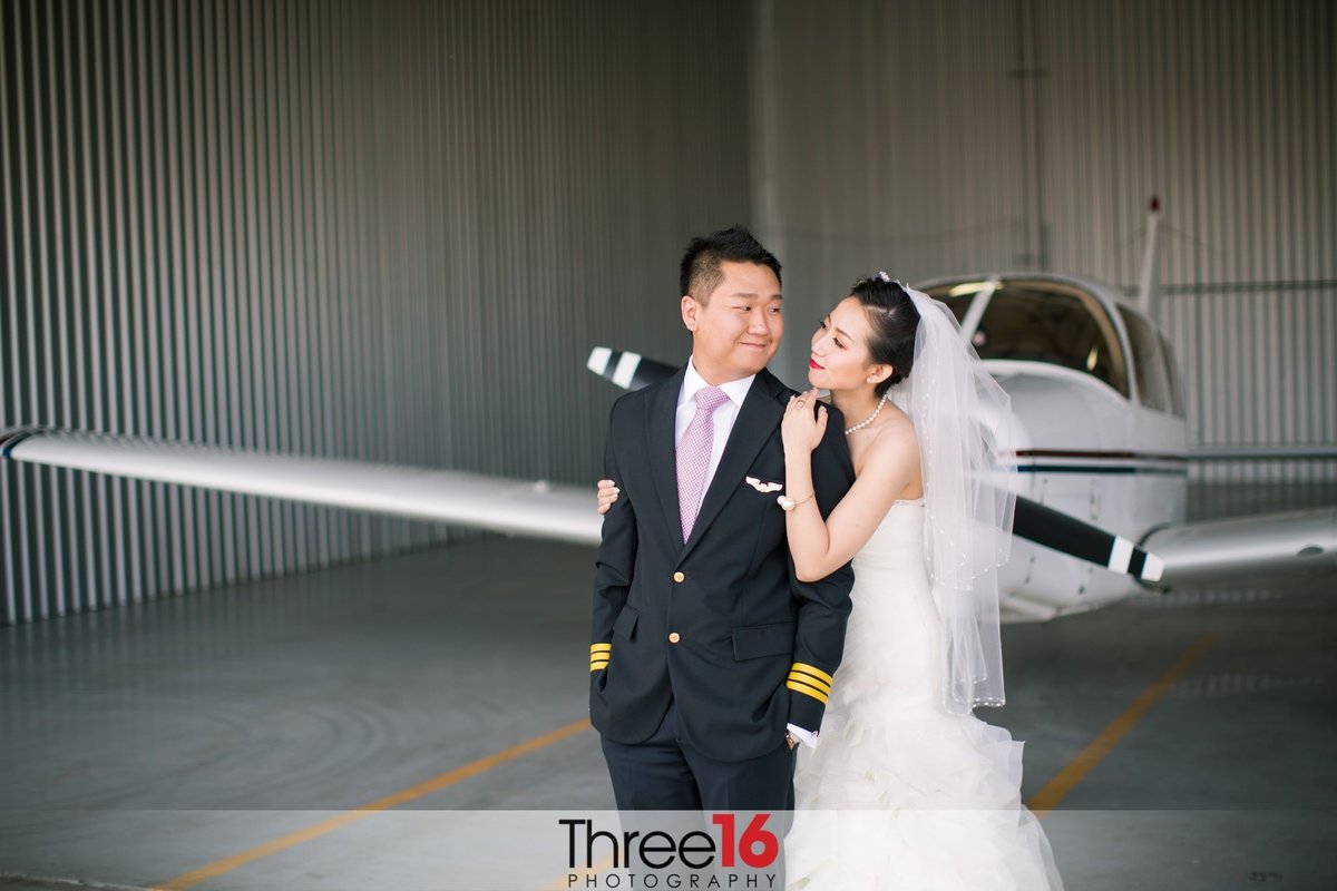 Bride and Groom cozy up to each other and gaze into each other's eyes in front of a plane inside a hangar