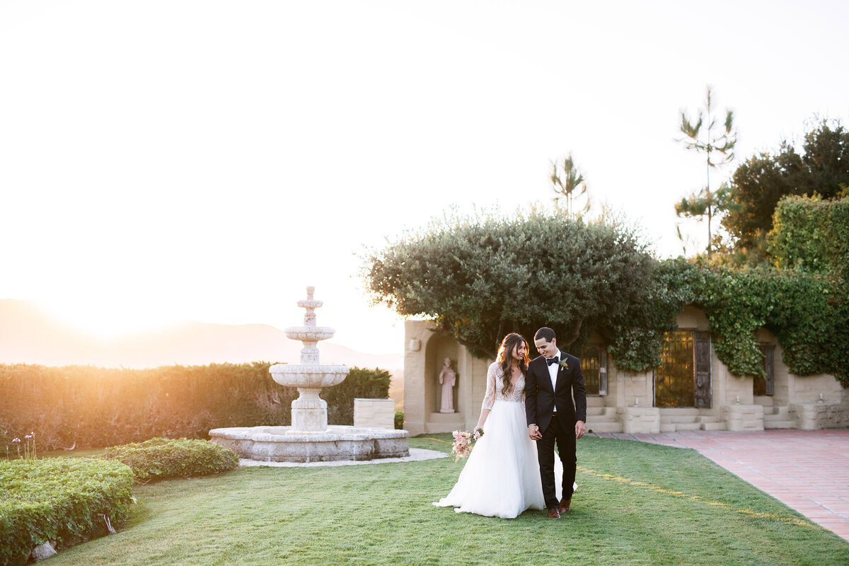 Bride and groom walk in ocean side garden at Whispering Rose Ranch at sunset