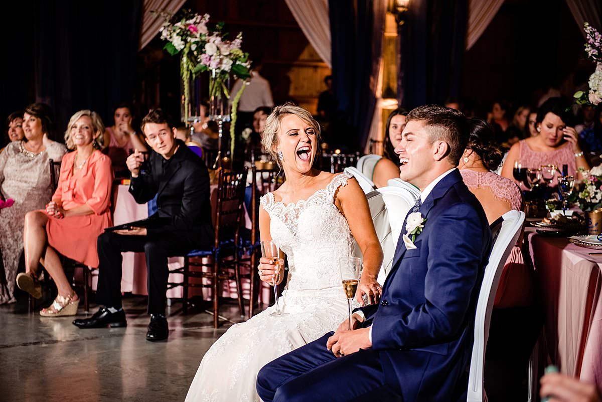 Bride laughing during reception speeches with her husband sitting beside her