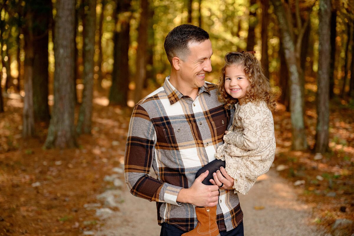 father dressed in a plaid shirt smiles at his daughter dressed in cream with curly dark hair