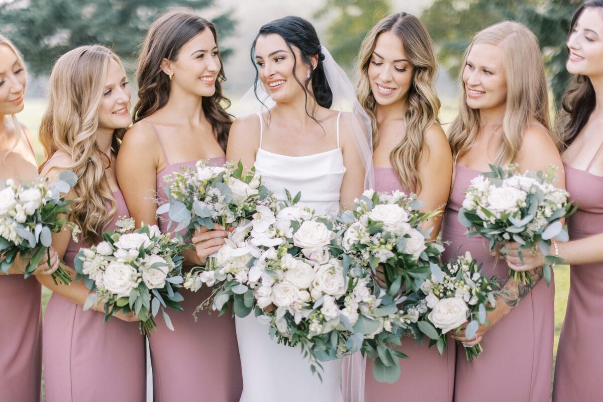 a group of brides maids with the brides in pink dresses holing flowers during a Calgary wedding photographed by Alberta wedding photographers Heidrich Photography