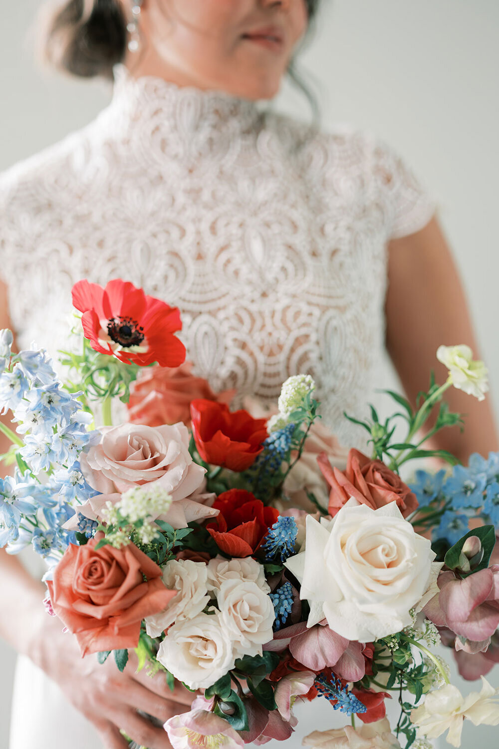 Bride holding a modern wedding bouquet with red poppies, blush and ivory roses, and blue delphinium, captured at the Kimpton Armory in Bozeman for a modern wedding inspiration shoot.