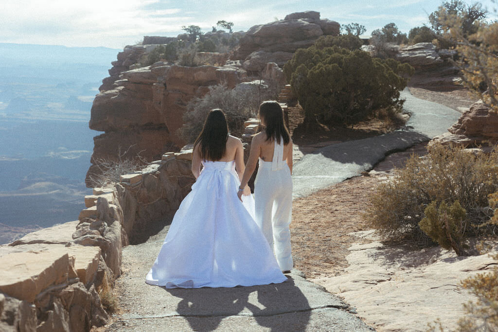 A wedding couple holding hands and walking along a trail.