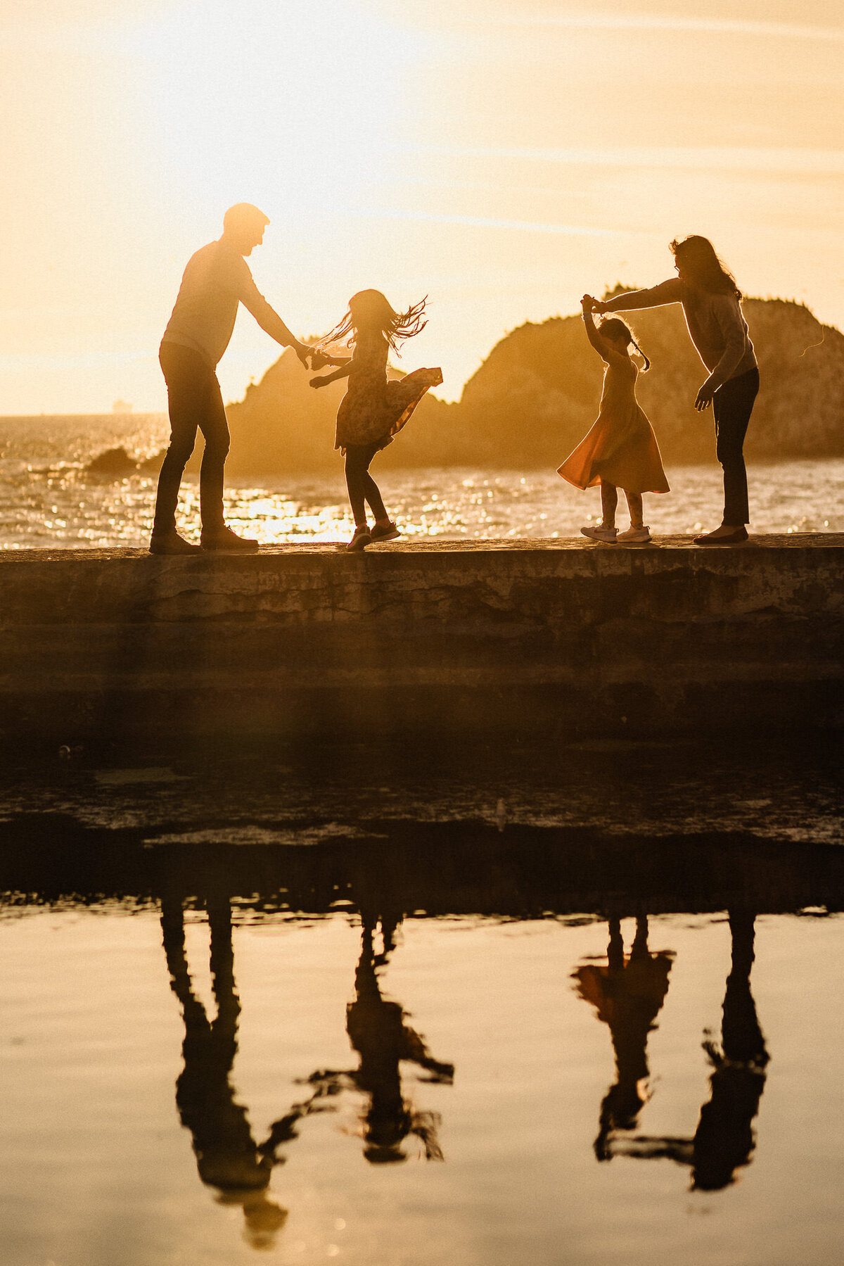 Silhouette family portrait dancing on Sutro Baths during sunset