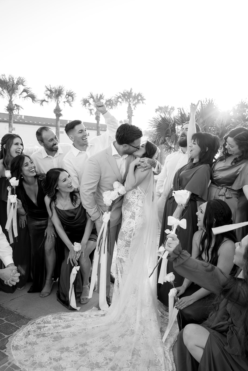 Bride and groom kiss surrounded by joyful bridal party during a micro-wedding at Casa Marina Hotel in St. Augustine, Florida, captured in black and white digital by The Detablans