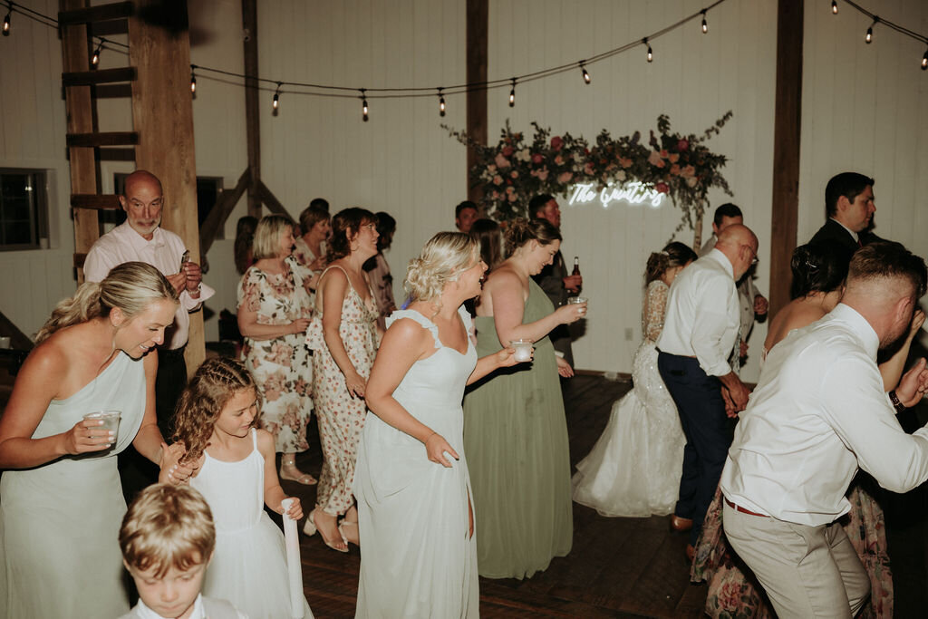 guests dressed in white and sage green dancing inside the modern barn at Willowbrook wedding venue