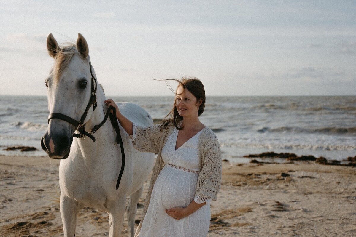 Femme enceinte tenant son cheval face à la mer, cheveux au vent. Par Kamescop, photographe en Bretagne.