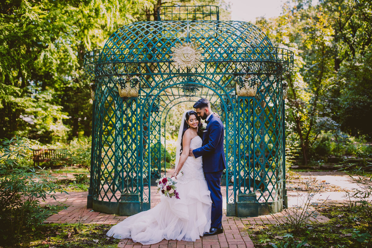 Indian christian bride and groom outside a green birdcage gazebo at the thielke arboretum in glen rock nj