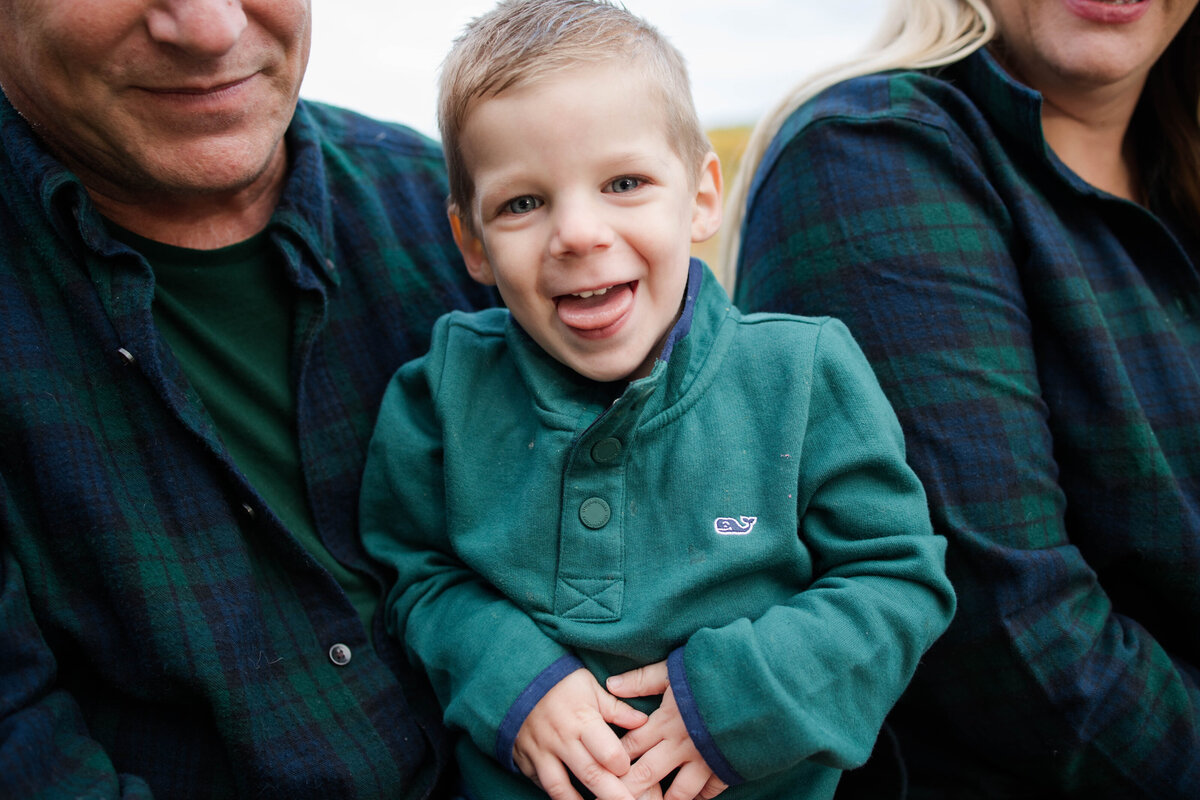 toddler boy laughing and sticking his tongue out at the camera as mom and dad hold him