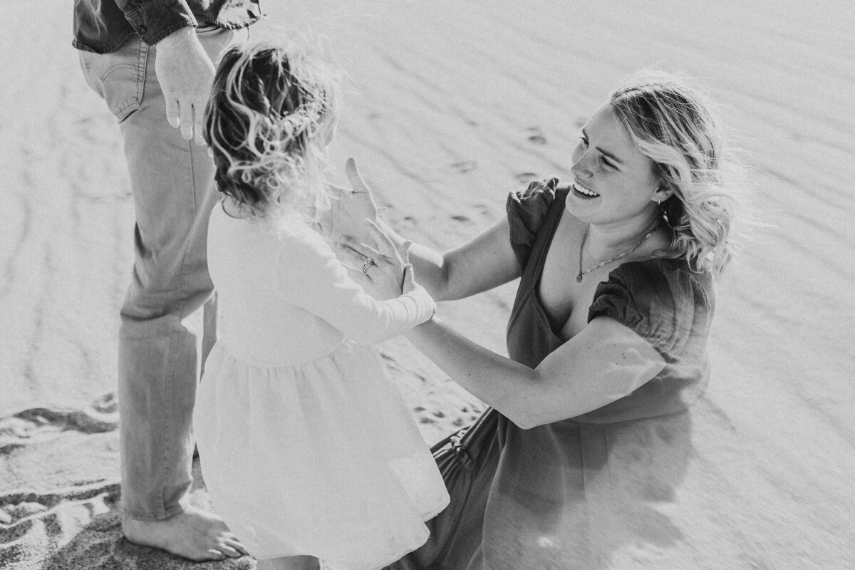 A mother gently strokes her daughters face while sitting in the sand.