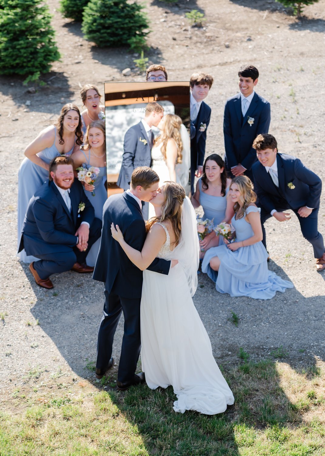 bride and groom kiss in front of mirror surrounded by wedding party