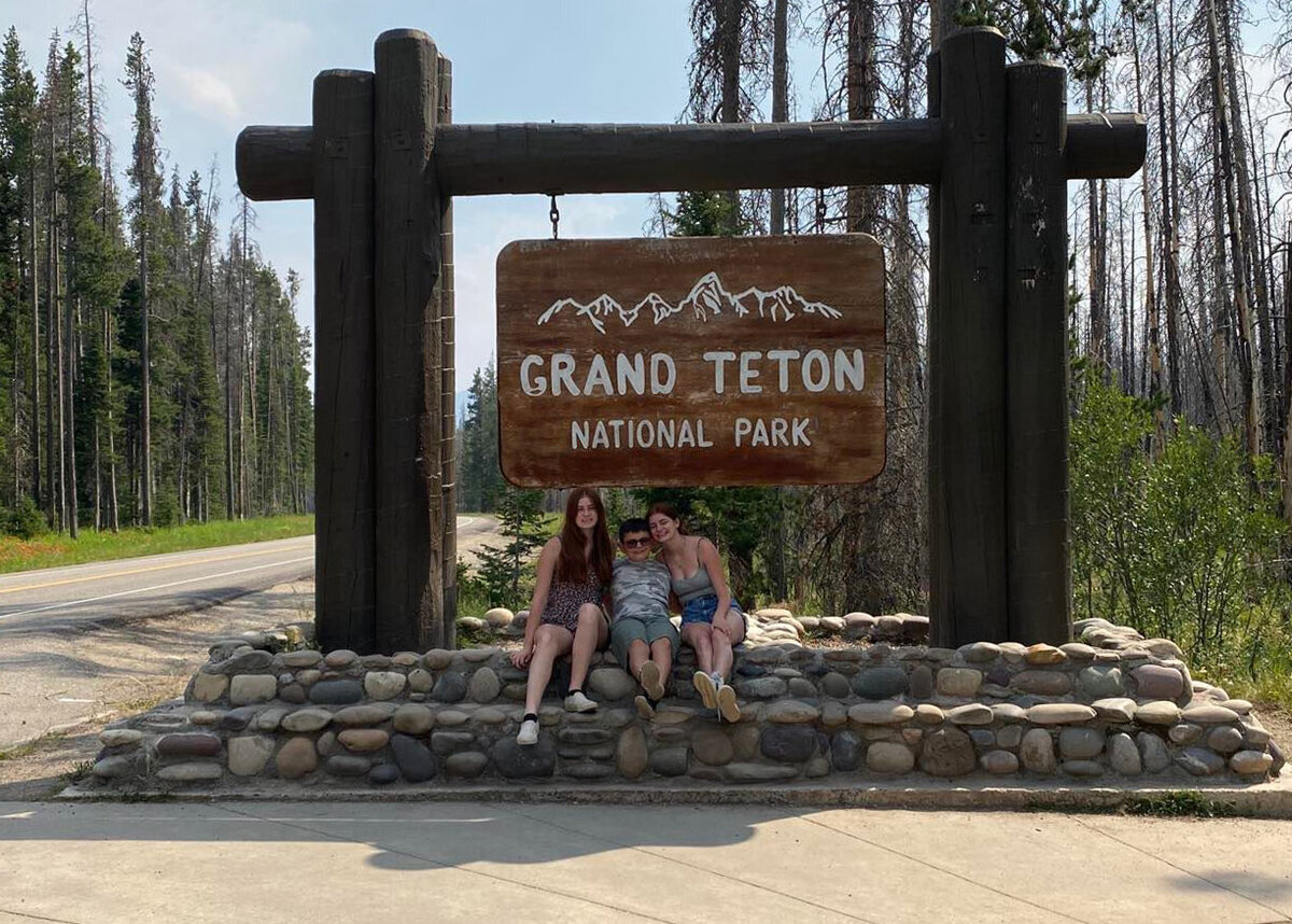 three kids sitting in front of a grand teton sign in the smokey mountains