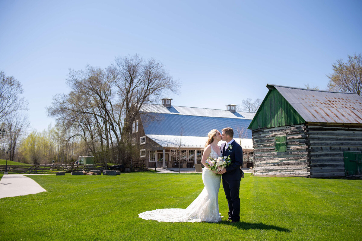 a bride and groom kiss outside with the Stonefields Estate Loft and barns in the background