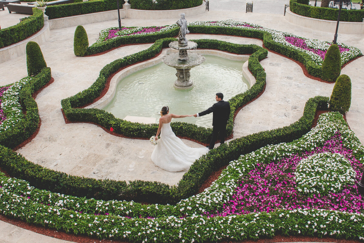 Bride and groom hold hands walking around a beautiful courtyard fountain in Miami.