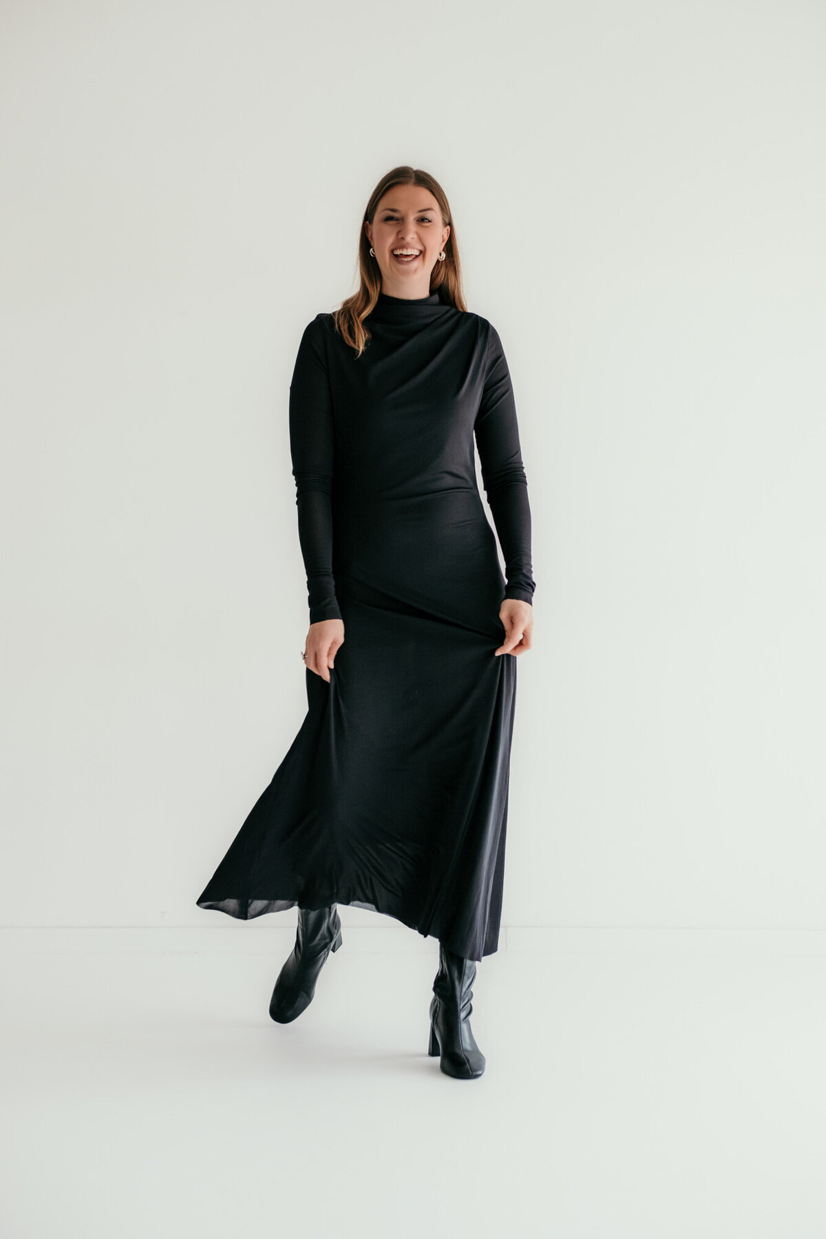 Woman in a long black dress laughs at the camera.