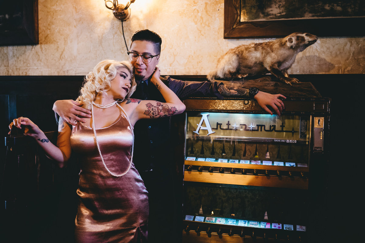 Engaged couple leaning on vintage cigarette vending machine that now vends art