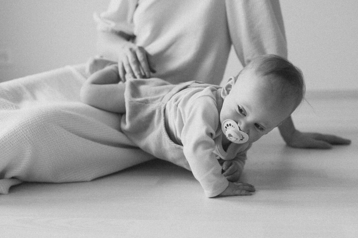 Mother sitting on the floor and her child climbing over her legs at home in Helsinki