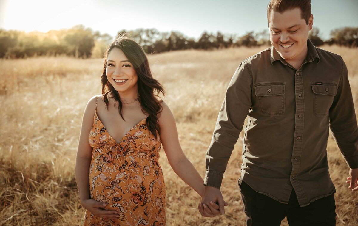 Man holding his pregnant wife's hand while they walk  towards the sunset