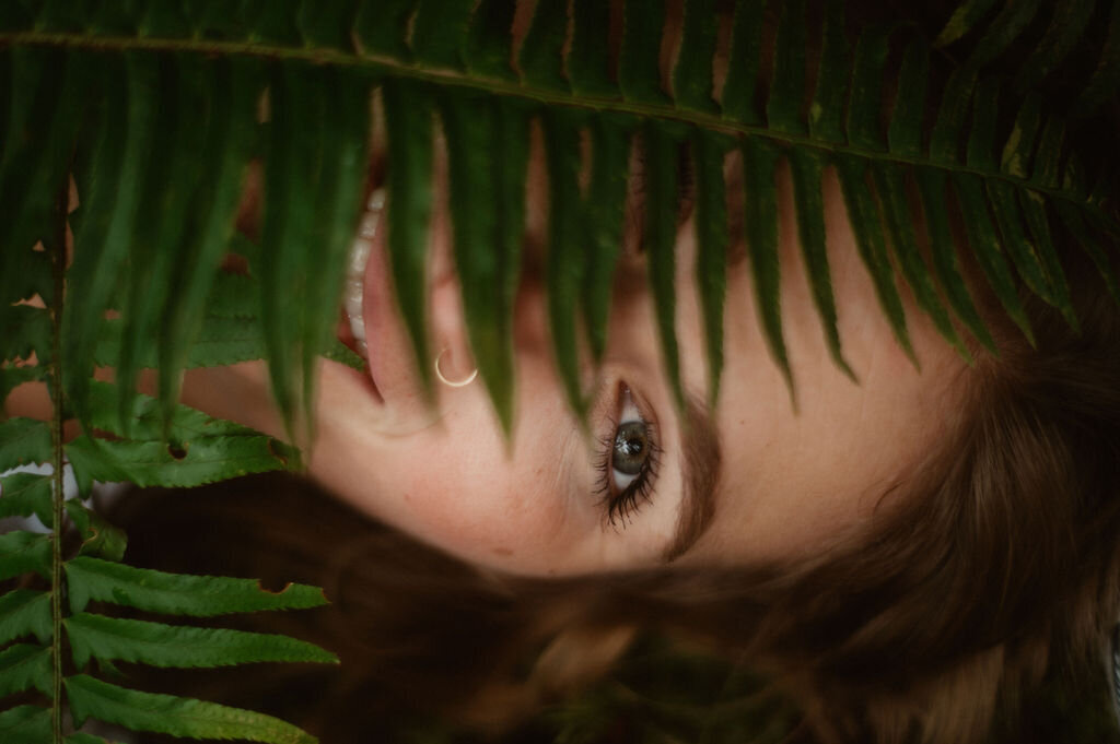 portrait of women laying  in forest with fern over her face