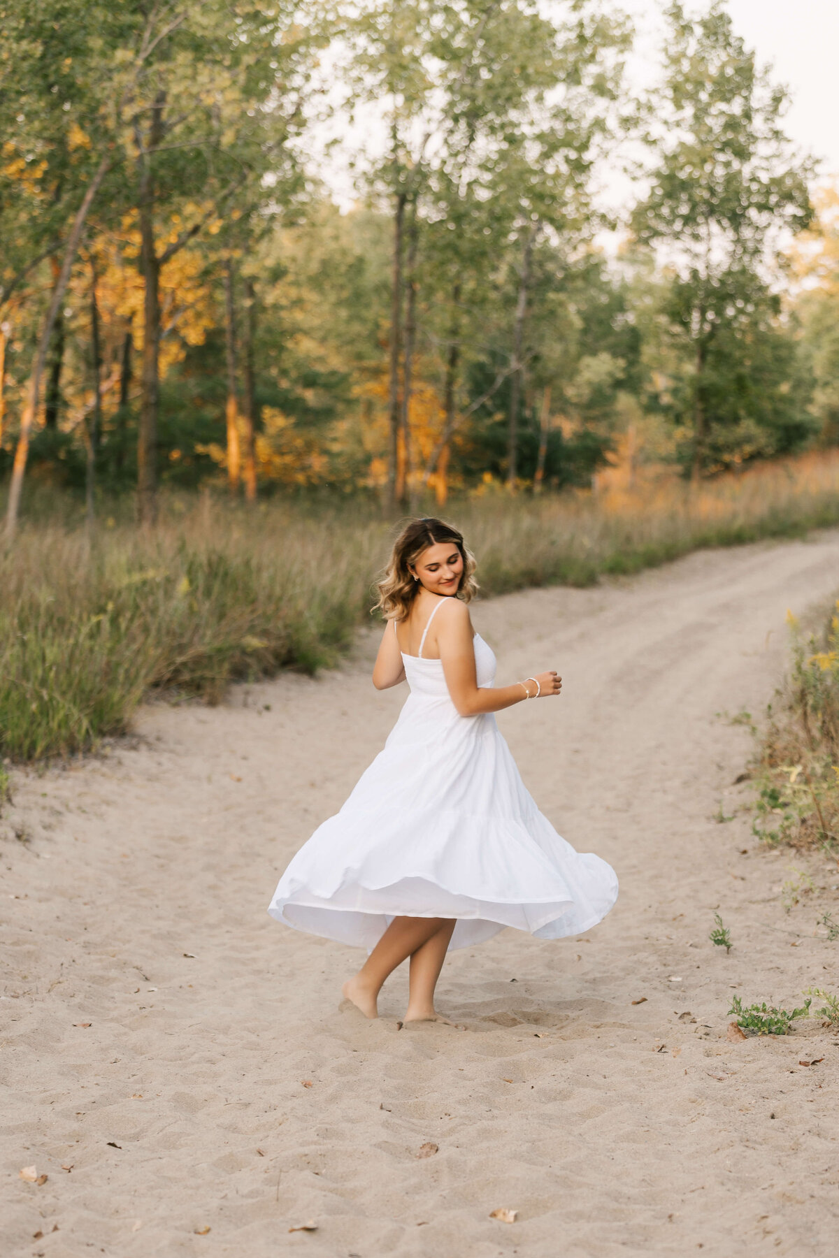 Photo of a high school senior twirling in a white dress in the sand at a beach in Erie Pa