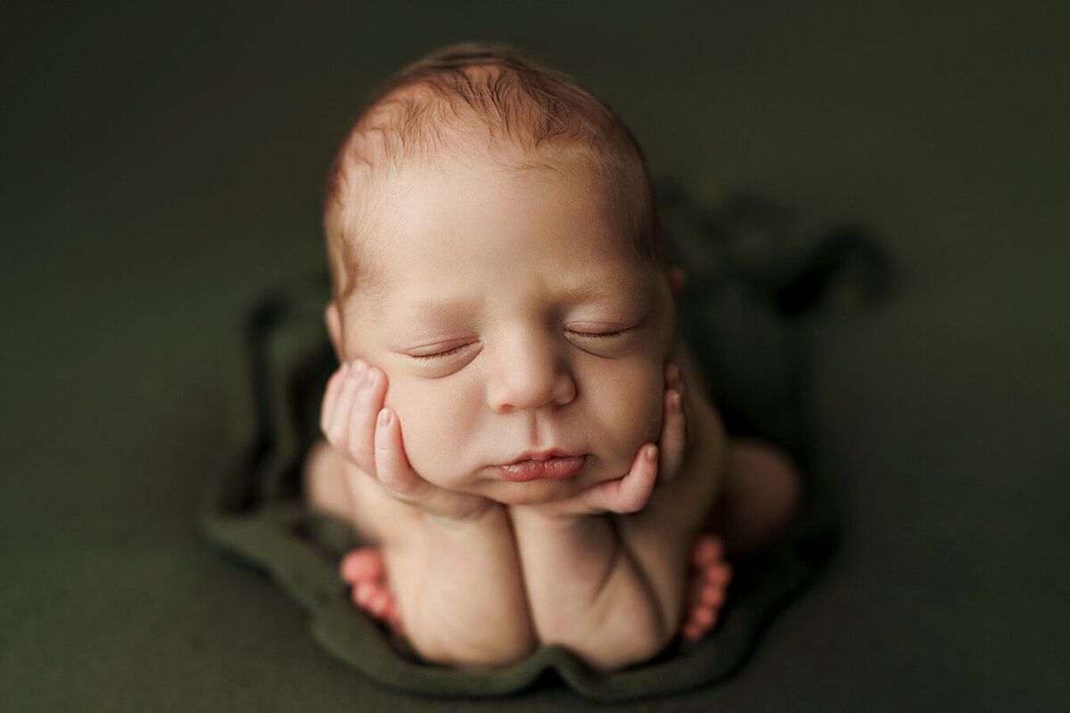 Adorable newborn baby boy holding his head in his hands in the froggie position