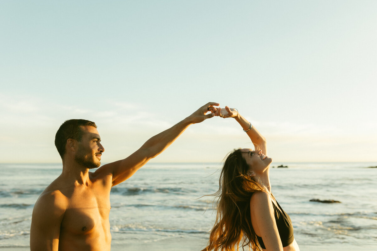 A guy spinning a girl by her finger near the ocean.