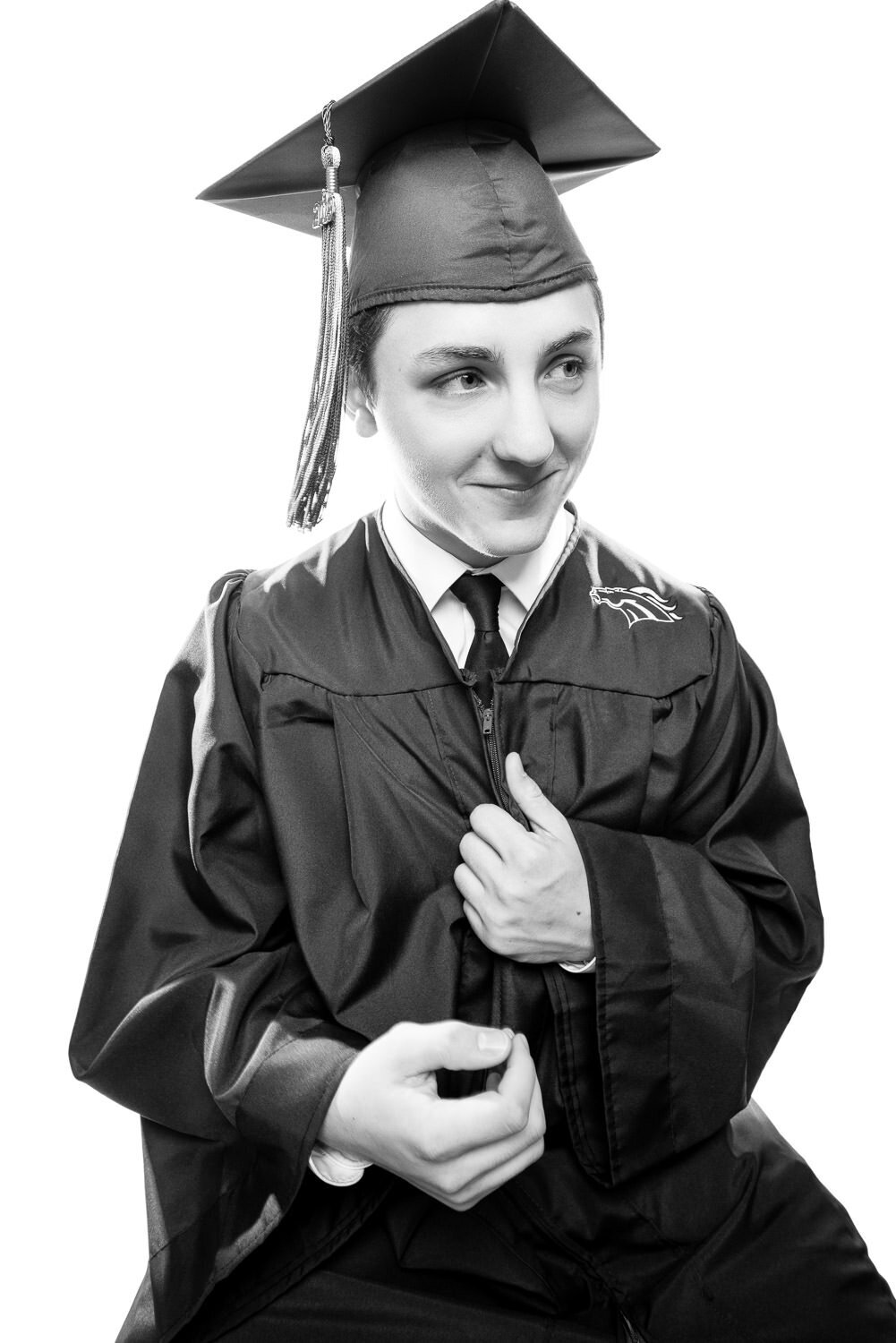 High-key editorial portrait of a male graduate in cap and gown, photographed in a clean, modern studio style.