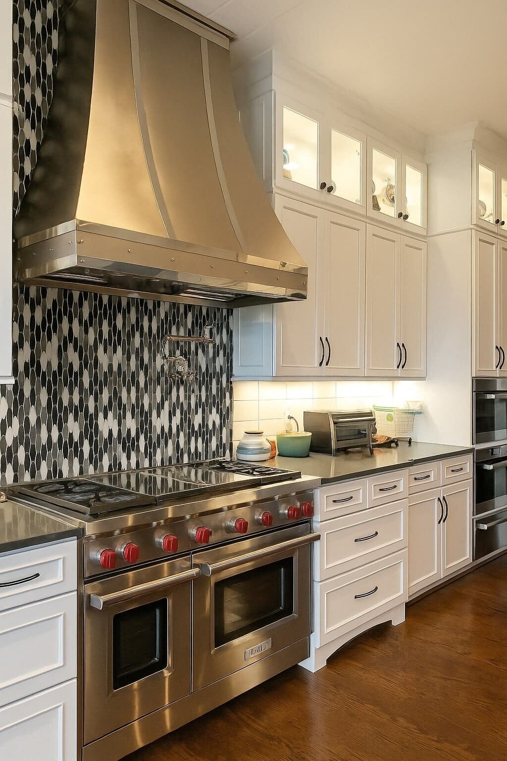Modern kitchen renovation featuring a stainless steel range hood, Wolf double oven, white cabinetry, and black-and-white mosaic tile backsplash.