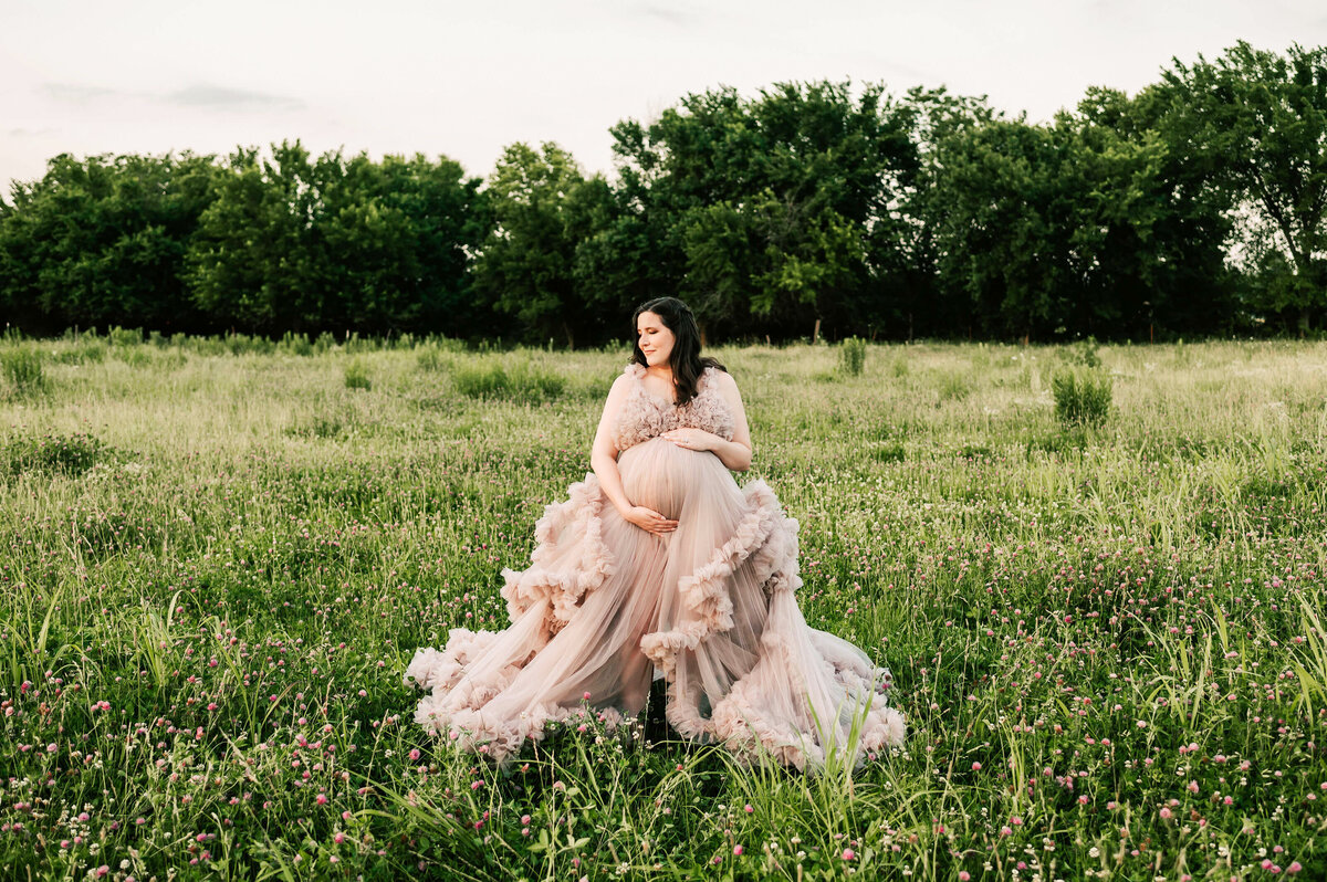 pregnant mom in purple dress holding baby bump in a field of of flowers during Springfield MO maternity photogrpahy session