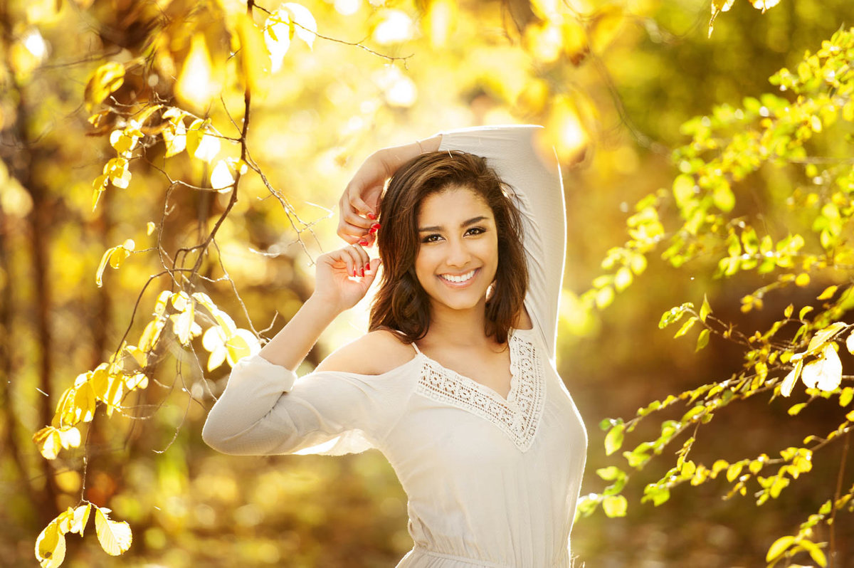 high school senior photo of girl in white dress with yellow fall leaves and sun