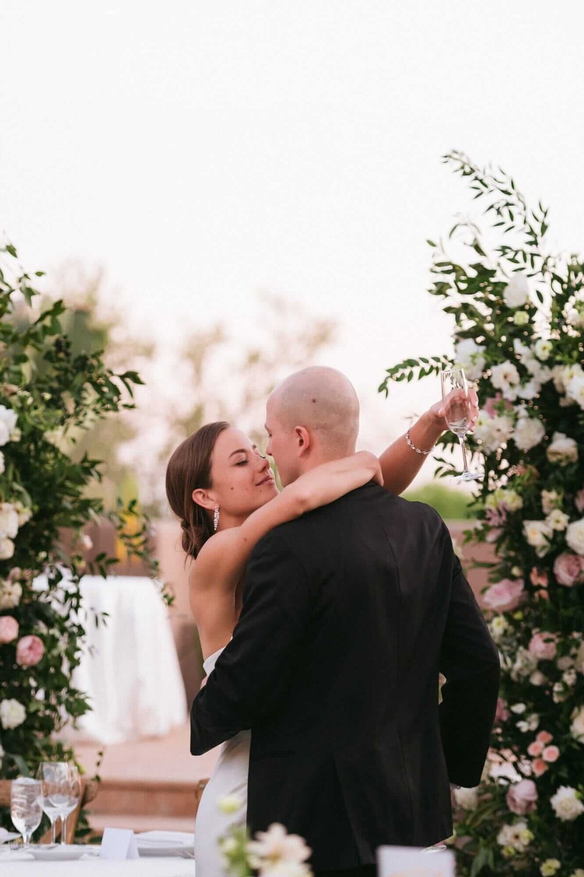 Bride raising her glass while embracing her groom during an elegant outdoor reception by Scottsdale wedding photographers in Arizona.