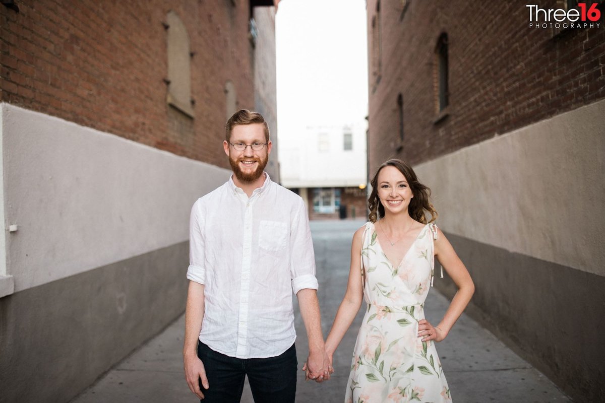 Engaged couple hold hands while standing in an alley way in Old Towne Orange