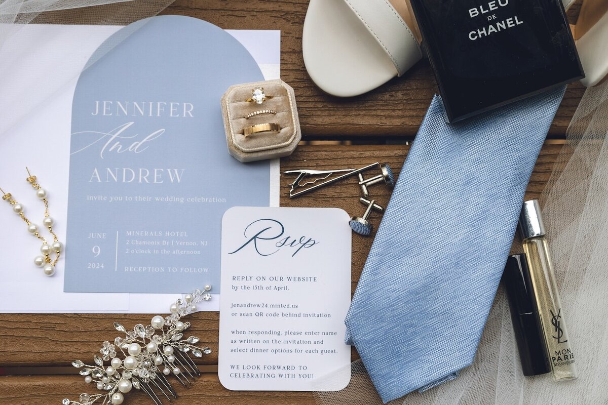 Flat lay of wedding invitations, blue tie, and wedding bands