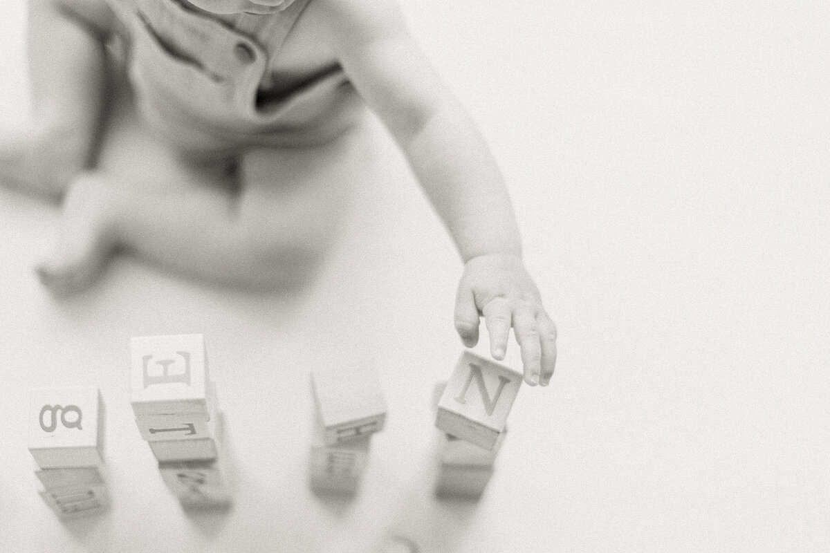 Close up black and white photo of a baby boy playing with some wooden blocks.