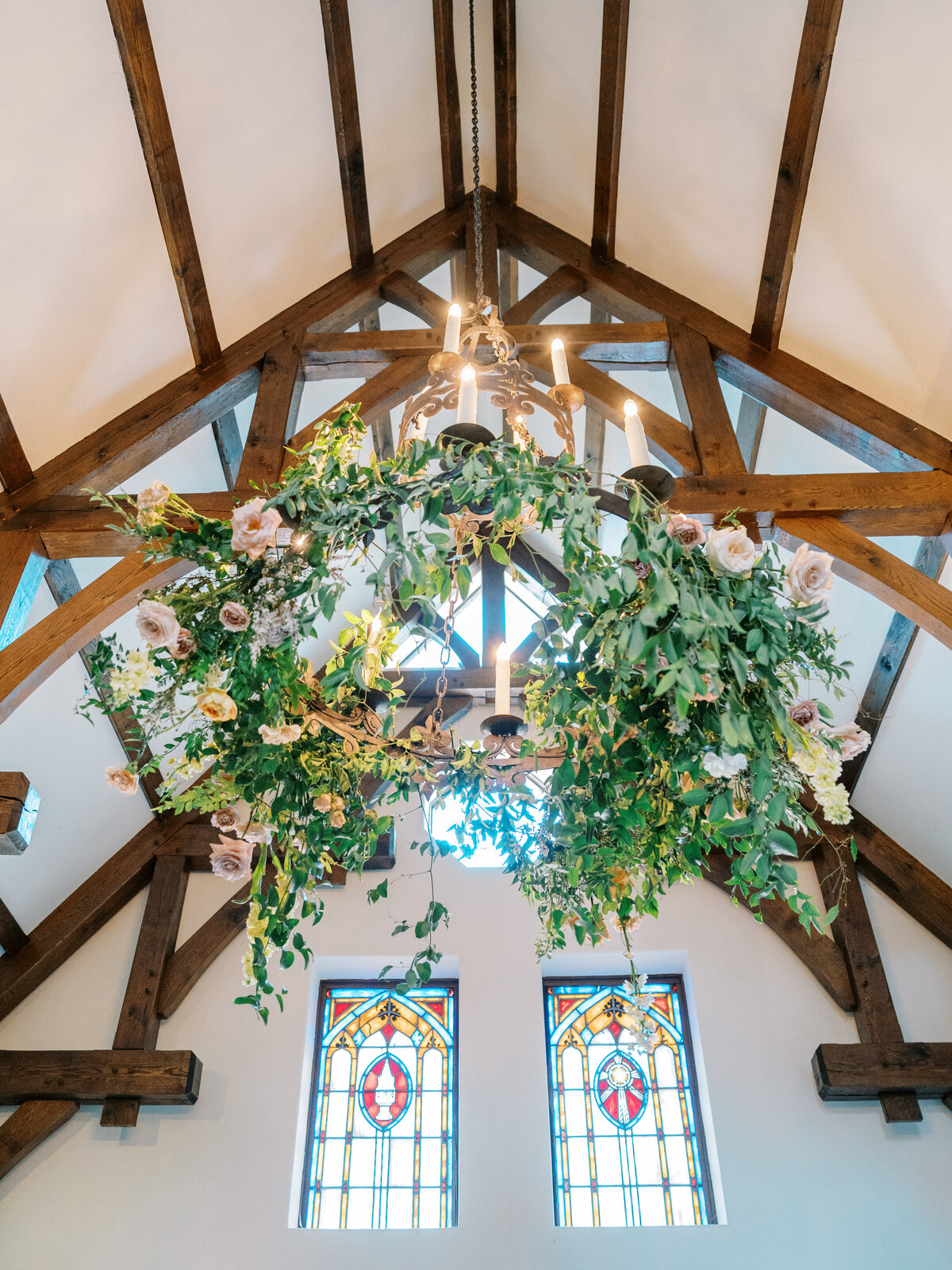 Floral chandelier installation with greenery and roses hanging above stained glass windows inside the Castle Ladyhawke ceremony space.