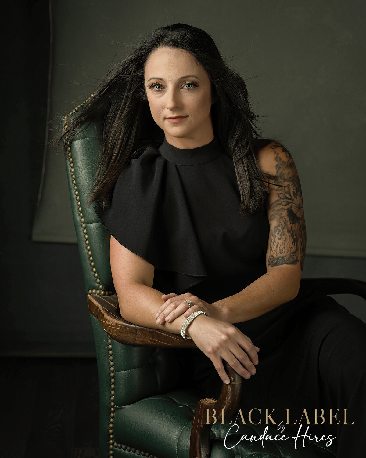 tattooed woman photographed in green leather chair on a black bakcdrops