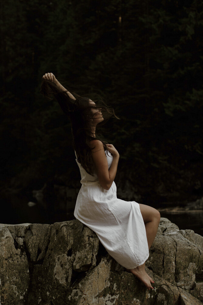 girl sitting on a rock in a white dress, letting her hair blow in the wind