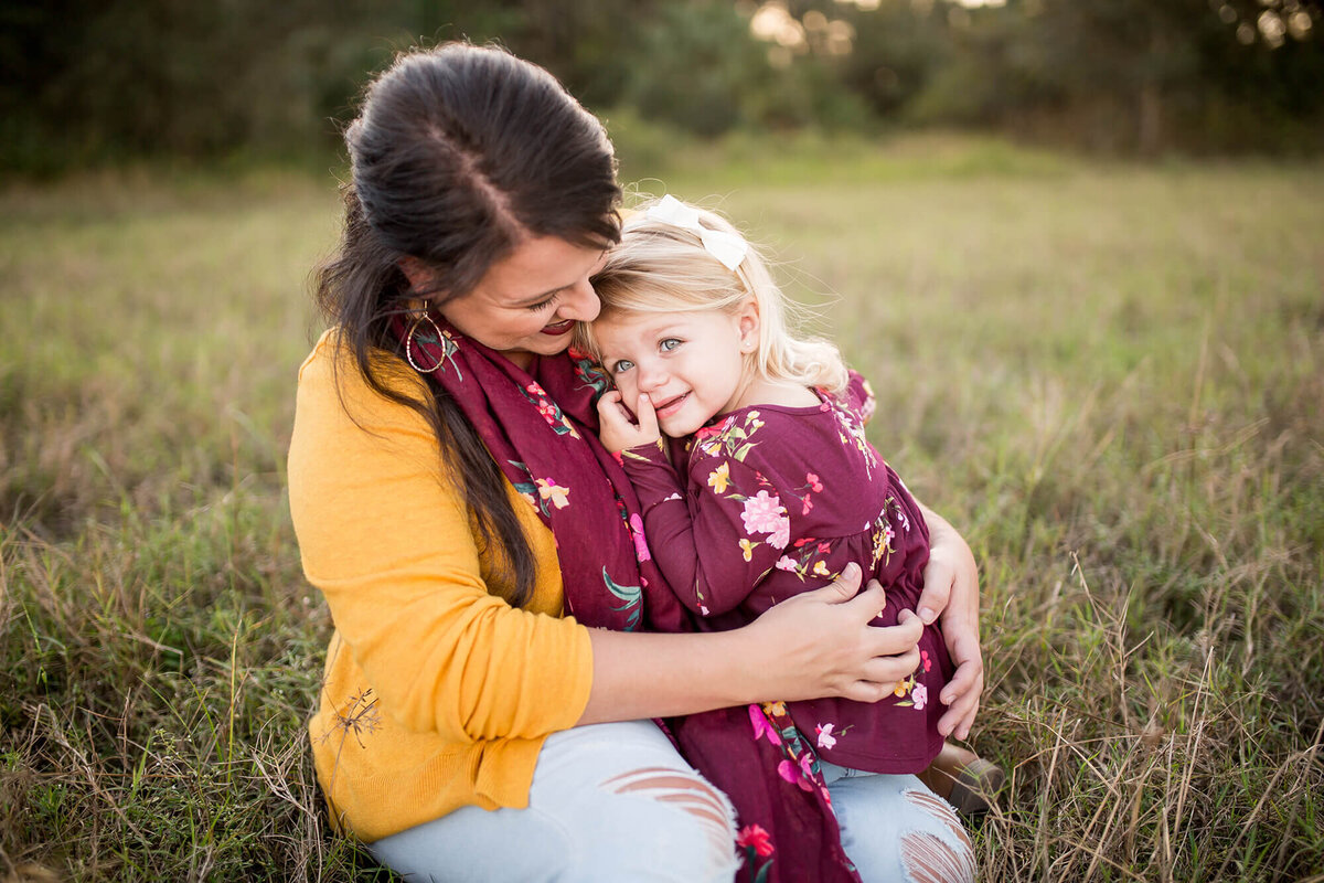 warm farm family portrait of mother daughter cuddling in tall grass located in South Tampa, FL 