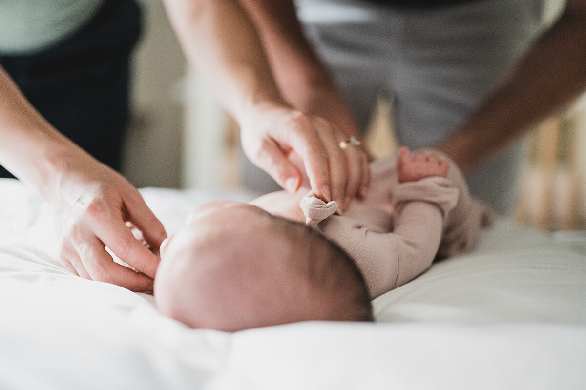 Parents dressing newborn on bed during documentary-style session in Connecticut home